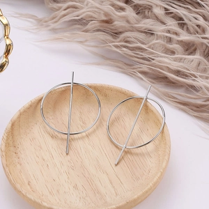 Macro detail of geometric silver oval earrings on a light wooden tray with soft textures