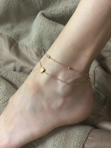 Close-up of golden double-layer anklet with heart charm and small beads on ankle