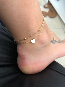 Close-up of golden double-layer anklet with heart pendant and bead chain on woman's ankle