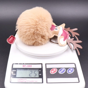 Close-up of cute Christmas reindeer plush pompom keychain weighing 25g on a scale