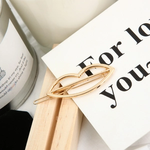 Close-up of golden lip-shaped metal hair clip on a minimalist white card and wooden stand