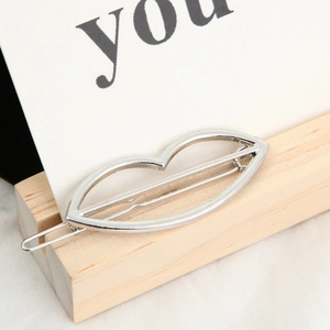 Detail of silver hollow lip-shaped metal hair clip on a minimalist wooden display stand