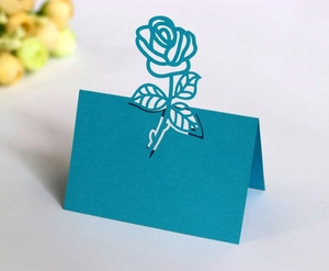 Detail showing the intricate laser-cut rose design on a blue paper wedding place card