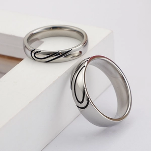Silver titanium steel couple rings with black engraved heart pattern on geometric stand