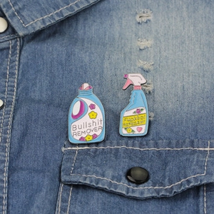 Detailed close-up of funny enamel pins with laundry spray design on denim fabric