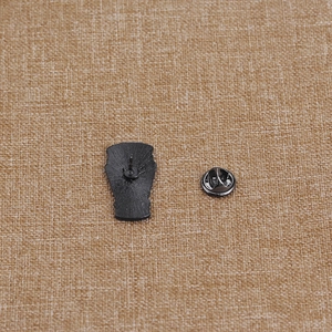Black coffin enamel pin with textured finish and butterfly clasp on linen background