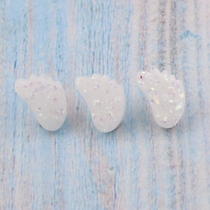 Detailed macro view of three white resin tiny foot-shaped beads with glitter finish