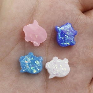 Close-up of small pig-shaped opal beads in four colors held in a palm for scale