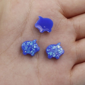 Macro shot of three blue pig-shaped synthetic opal beads held in palm for DIY jewelry
