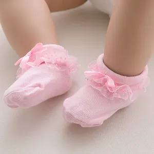 Close-up of pink baby sock featuring polka dot lace ruffles and a silk ribbon bow detail