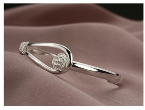 Detailed close-up of a silver cherry blossom open bangle on purple pleated fabric