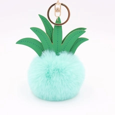 Detail of pineapple keychain with green leather leaves and light blue fluffy fur pompom
