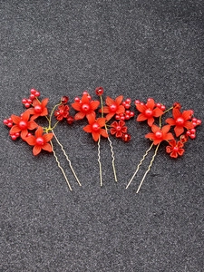 Detailed view of three red bridal flower hair pins with pearls and golden accents