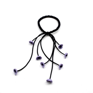 Detail of black spiral hair tie with dangling light purple flower pendants on white background