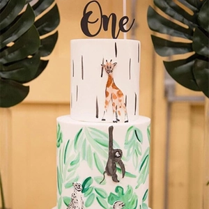 Close-up of black 'One' acrylic cake topper on a jungle animal themed birthday cake