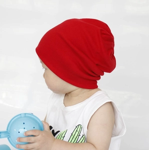 Side view of a bright red cotton knit beanie for kids on a young model with plain background