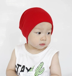 Close-up of baby wearing a bright red cotton knit beanie hat against a white background