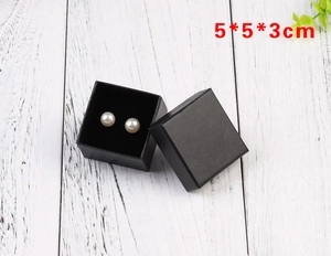 Detail view of black 5x5x3cm square jewelry box with textured surface and pearl earrings