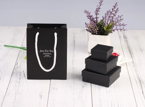 Macro shot of matte black jewelry gift boxes and matching paper bag on a wooden surface