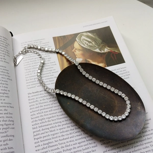 Dettaglio collana tennis in argento con zirconi brillanti appoggiata su un libro d'arte