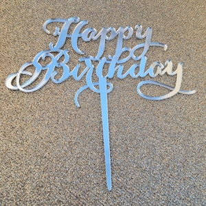 Macro shot of silver mirror acrylic Happy Birthday cake topper on gold glitter background