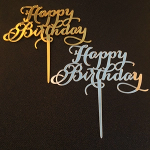 Detail view of gold and silver acrylic Happy Birthday cake toppers on a dark background