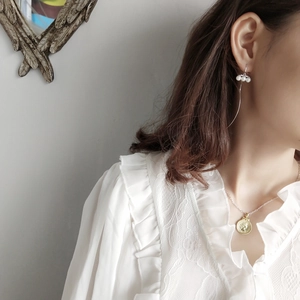 Elegant pearl drop earrings and gold coin necklace worn by model in a minimal setting