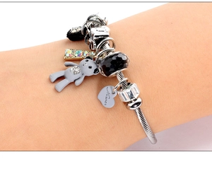 Detail of a silver stainless steel charm bracelet featuring bear and heart pendants