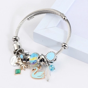 Close-up of DIY bear charm bracelet with blue swan and gold bow details on white