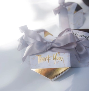 Macro shot of hexagon marble gift box with gold foil patterns and grey ribbon bow
