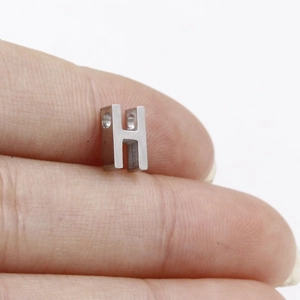 Macro shot of a small silver stainless steel letter H slider bead held between fingers