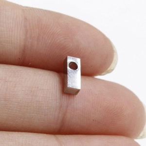 Macro shot showing the size of a small stainless steel rectangular charm with a top hole