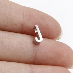 Macro shot of silver stainless steel letter J pendant on finger showing small size