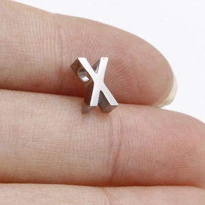 Macro shot of silver X-shaped stainless steel bead pendant displayed on a fingertip