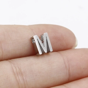 Macro shot of silver stainless steel letter M bead for DIY jewelry making on finger