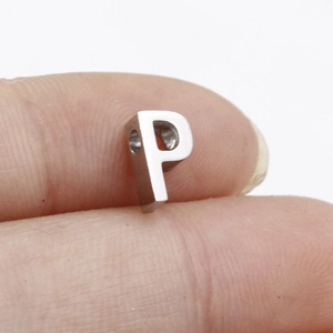 Close-up of a silver letter P metal pendant being held by fingers for scale
