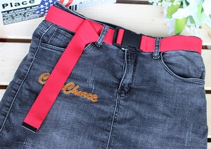 Detail of red woven belt with black plastic buckle on grey denim skirt