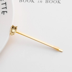 Detail of a golden owl hairpin with rhinestone eyes on a minimalist background