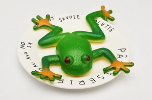 Macro shot of green toy frog with orange webbed feet on a white decorative plate