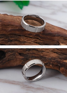 Detail of two silver titanium rings with brushed finish and vertical grooves on marble surface