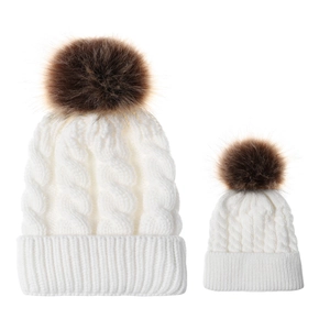Detail view of cable knit pattern and faux fur pom-poms on white parent-child beanies