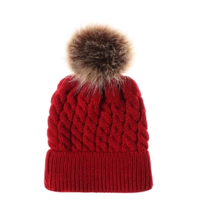 Close-up of red cable knit hat texture with a fluffy faux fur pom-pom detail