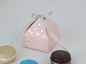 Detailed view of a pink polka dot pyramid candy box with a silver ribbon and macarons