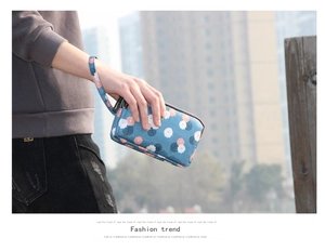Close-up of a three-layer floral canvas wallet with a wristlet held by a model outdoors