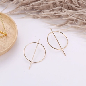 Detailed close-up of golden geometric stud earrings on a minimalist wooden tray