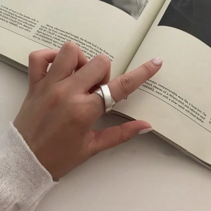 Minimalist matte 925 sterling silver crossover ring on finger with fashion magazine backdrop