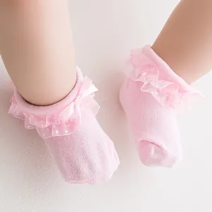 Close-up of pink baby socks with delicate lace trim, white dots, and a sweet bow detail