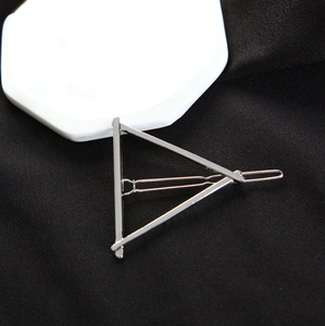 Close-up of a silver triangular metal hair clip on a minimalist black fabric surface
