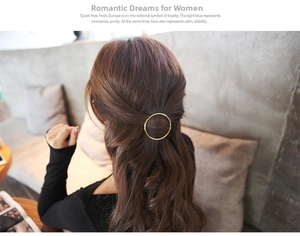 Close-up of a minimalist golden circular hair clip worn on long wavy brown hair