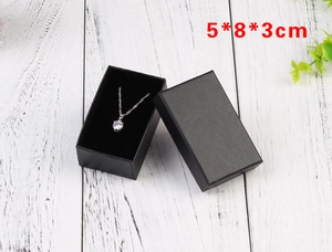 Top view of a black 5x8x3cm necklace jewelry box on white wood background with green plants